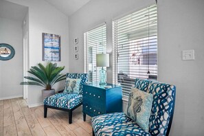 Une pièce comprenant deux fauteuils à motifs, une plante en pot, une armoire bleue et une lampe fixée au mur.