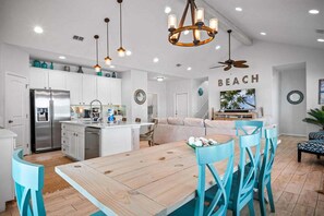 Una cocina moderna con armarios blancos, una isla central y un comedor con mesa de madera y sillas azules.
