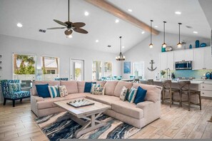 A spacious living room with a large beige sectional sofa, a coffee table, and a ceiling fan. - Island Gem- 4 BR Golf Cart Accessible Boardwalk (Port Aransas)