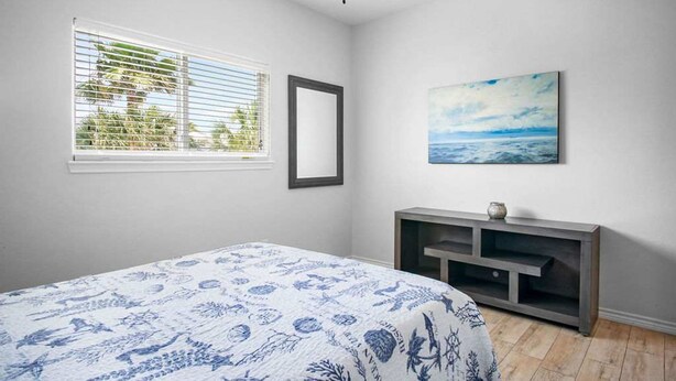 Un dormitorio con cama, ventana con persianas, un cuadro y un mueble para televisión.