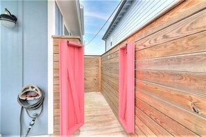 A narrow outdoor corridor with wooden walls, a metal gate, and a hose connected to a wall-mounted device. - La Puerta Rosada Private Pool Prime Location (Port Aransas)