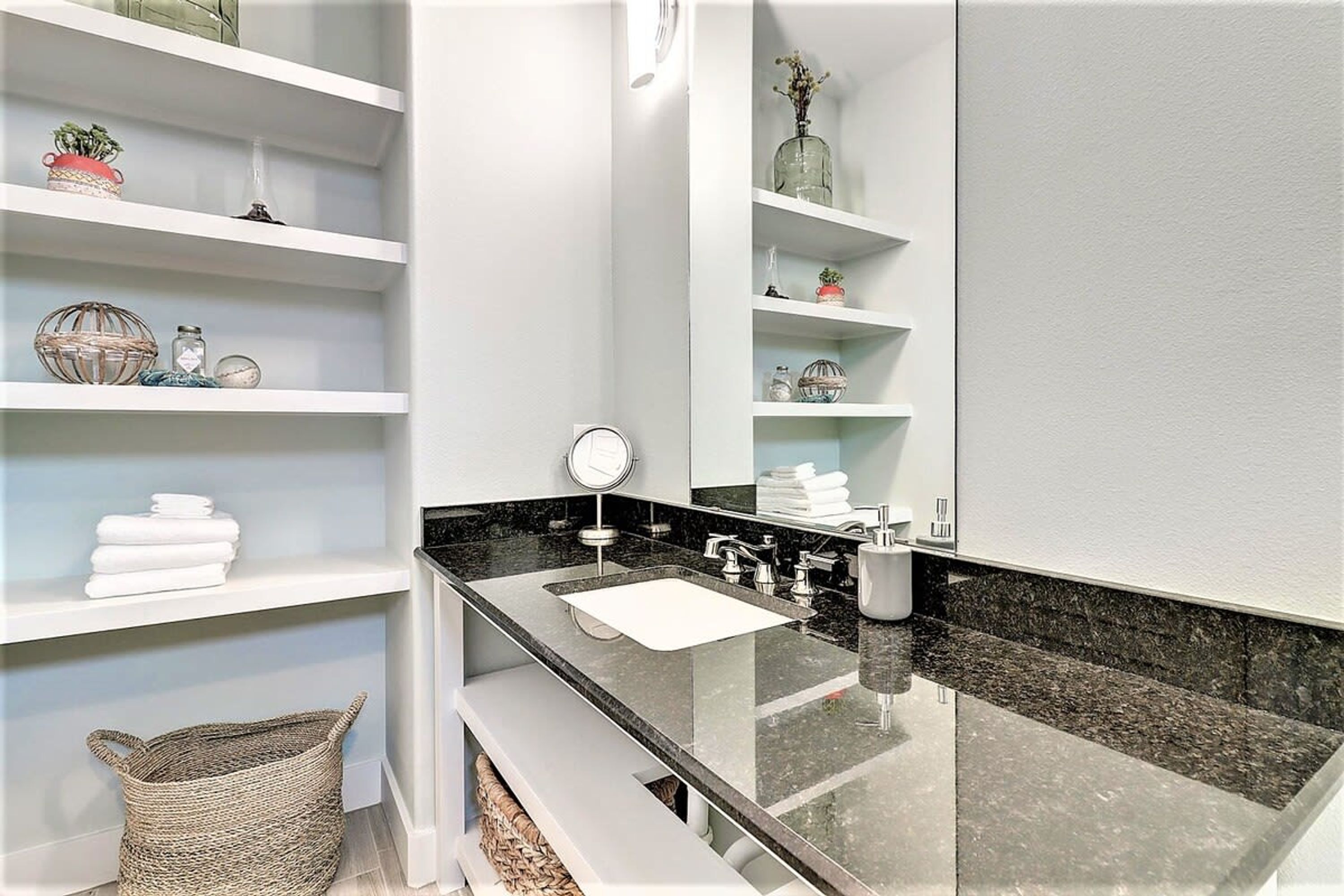 A modern bathroom with a black countertop, white shelves, and a large mirror.