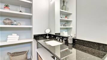 A modern bathroom with a black countertop, white shelves, and a large mirror.