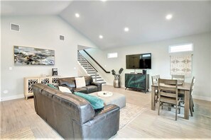 Ein modernes Wohnzimmer mit Ledersofa, einem Esstisch mit Stühlen, einem Flachbildfernseher und einer Treppe, die in eine obere Etage führt.