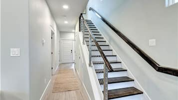 Un interior moderno con una escalera de madera, un pasillo y una puerta al final.