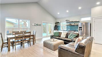 Uma sala de estar espaçosa com área de jantar, cozinha com painel azul e uma grande janela que oferece luz natural.