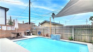 En trädgård med en pool, ett trästaket, en grill och en täckt uteplats.
