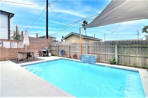 A backyard with a swimming pool, a wooden fence, a barbecue grill, and a covered patio area. - La Puerta Rosada Private Pool Prime Location (Port Aransas)
