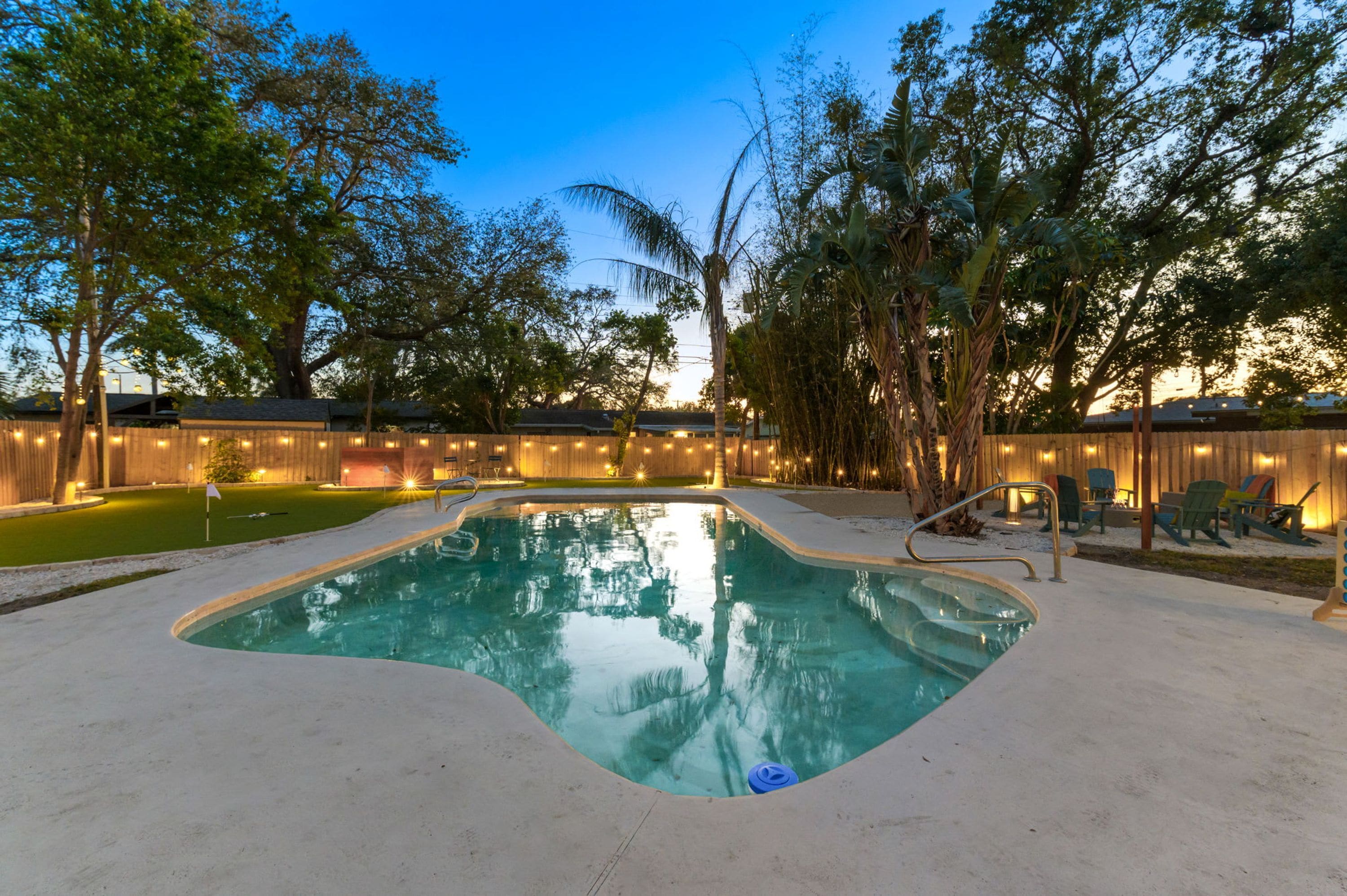 A swimming pool with a wooden deck, surrounded by trees and a wooden fence.