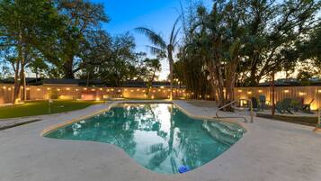 A swimming pool with a wooden deck, surrounded by trees and a wooden fence.