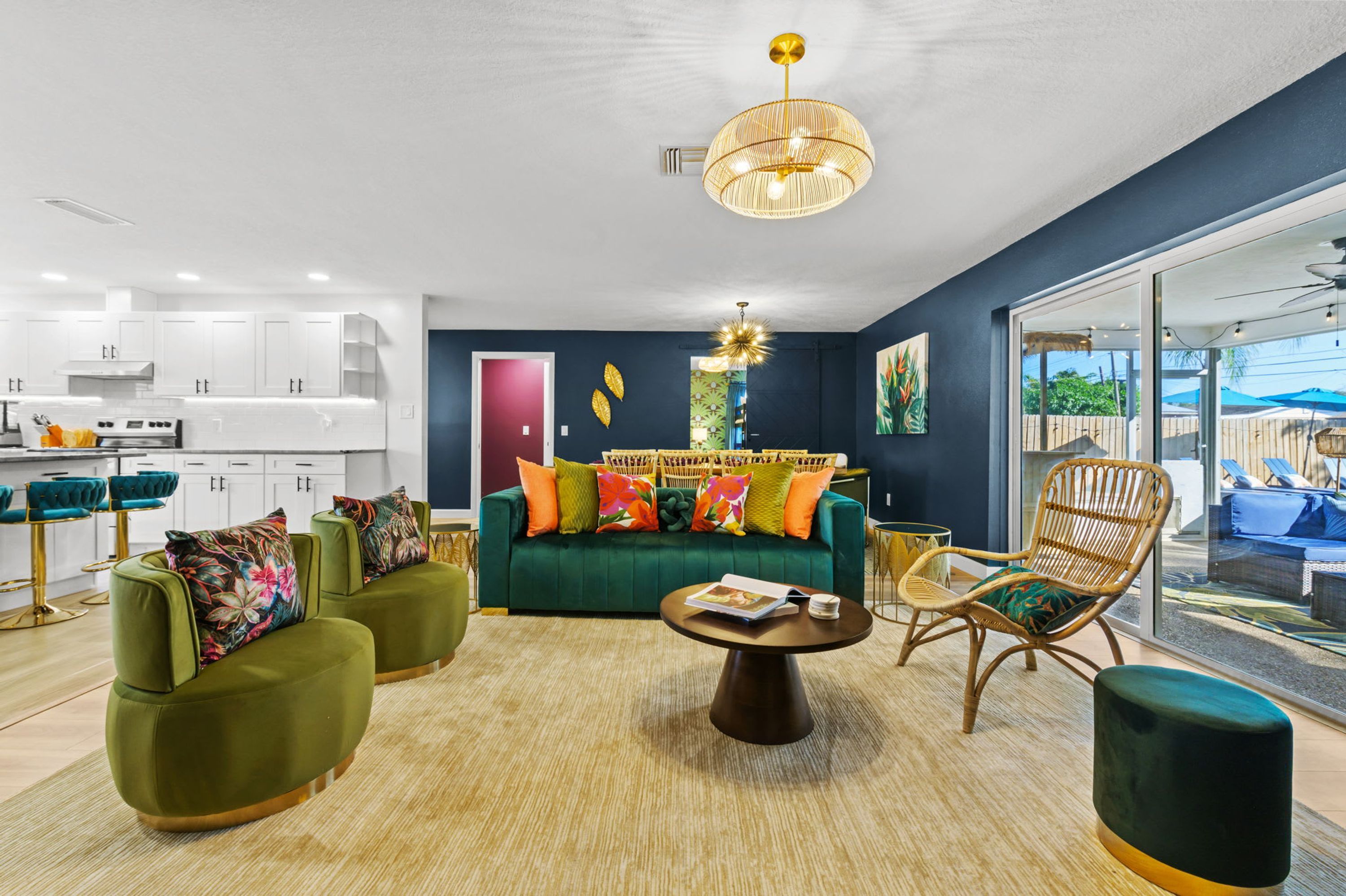 A modern living room with a green sofa, two armchairs, a coffee table, and a dining area with white cabinets and a kitchen.