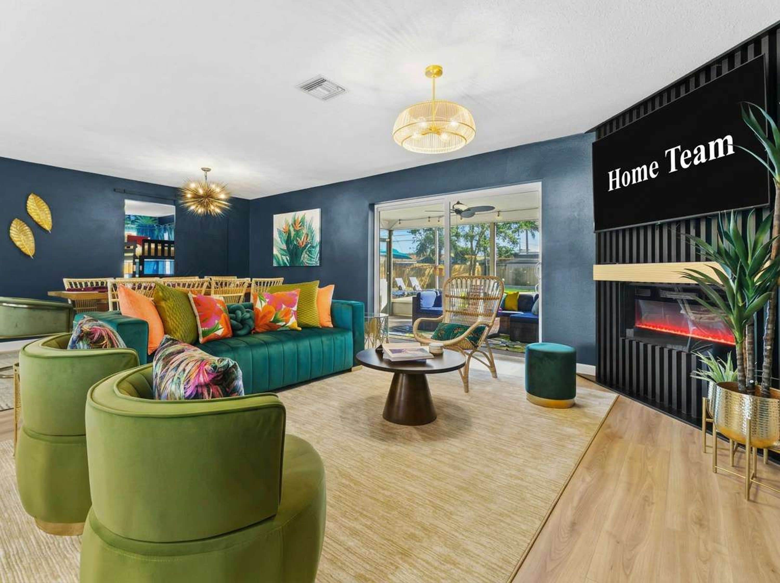A modern living room with a teal sofa, green armchairs, and a coffee table. There is a fireplace with a 'Home Team' sign on the wall.