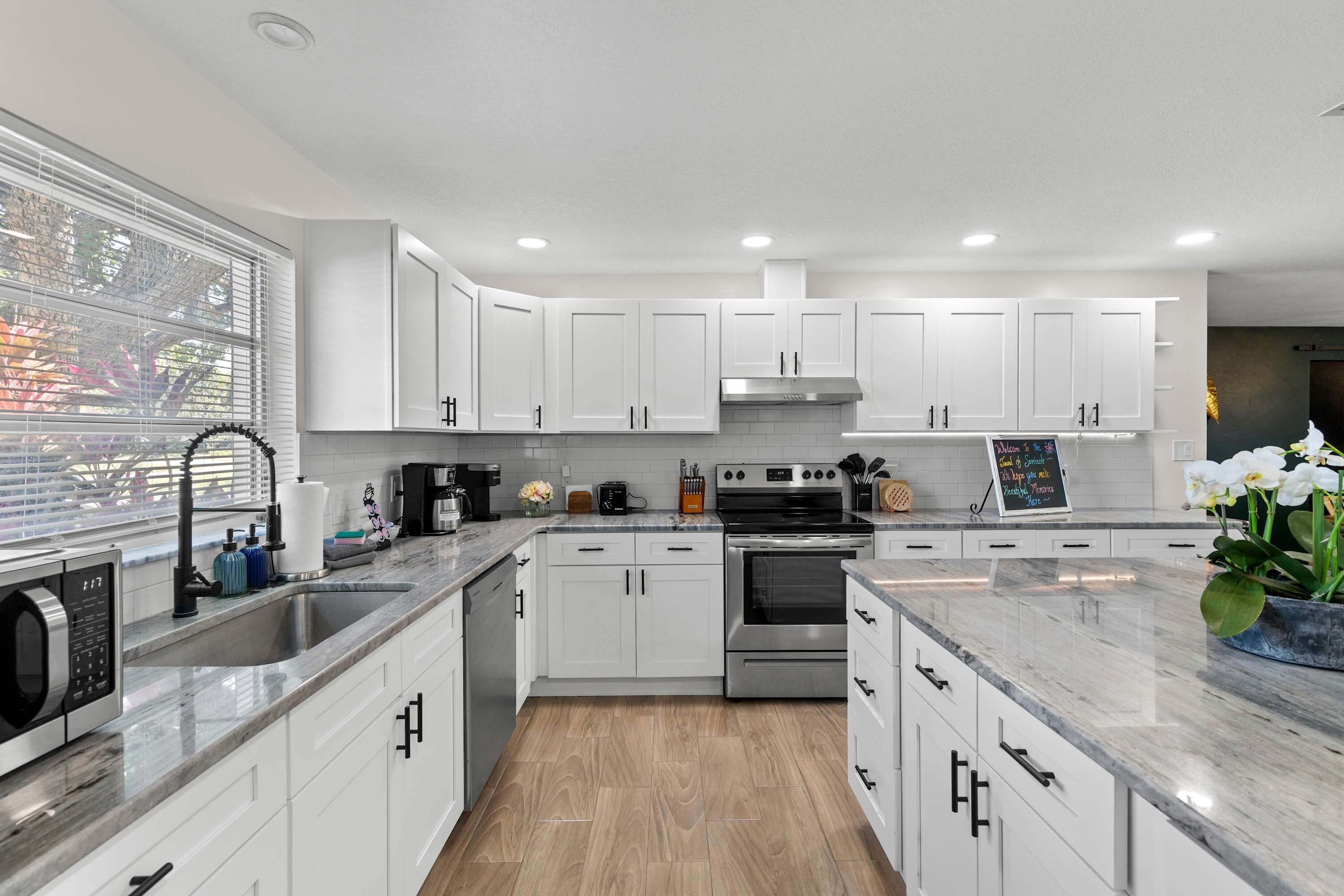 A modern kitchen with white cabinets, stainless steel appliances, and a marble countertop.