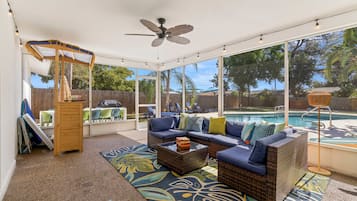 A covered outdoor seating area with a pool, wicker furniture, and a ceiling fan.