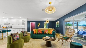 Un salon moderne avec un canapé vert, deux fauteuils, une table basse et un coin repas doté de meubles blancs et d’une cuisine.