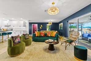 A modern living room with a green sofa, two armchairs, a coffee table, and a dining area with white cabinets and a kitchen. - 5 Min to Beach Heated Pool Golf Sleeps 12 (Seminole)