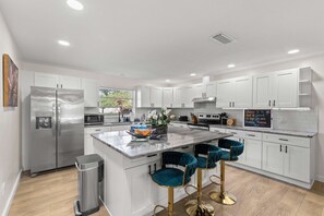 A modern kitchen with white cabinetry, stainless steel appliances, and a marble island with bar stools. - 5 Min to Beach Heated Pool Golf Sleeps 12 (Seminole)