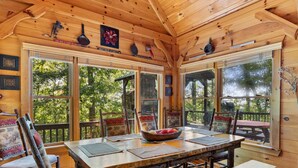 A wooden cabin interior with a dining table, chairs, and large windows offering a view of the outdoors. - Views for Miles Outdoor Fireplace Hot Tub (Morganton)