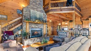 A cozy cabin interior with a stone fireplace, wooden furniture, and a staircase leading to an upper level. - Views for Miles Outdoor Fireplace Hot Tub (Morganton)