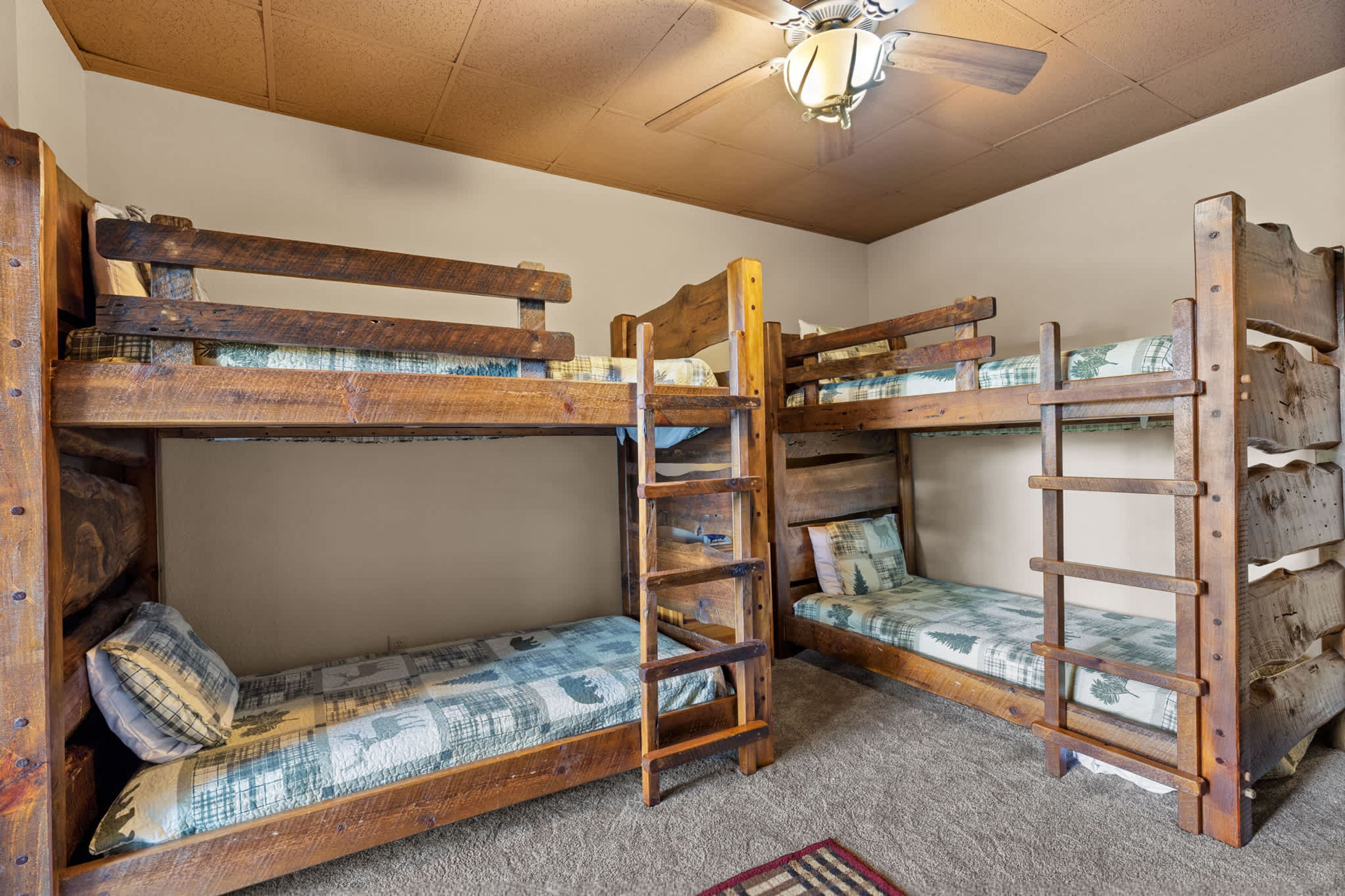 A bunk bed room with a ladder, a ceiling fan, and a patterned rug.