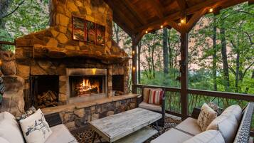 A stone fireplace with a fire, surrounded by outdoor seating with cushions.