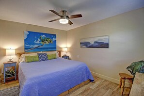 Ein Schlafzimmer mit einem Bett, zwei Nachttischen, einem Deckenventilator und zwei Bildern an den Wänden.