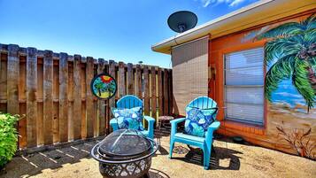 A backyard with a barbecue grill, two blue chairs, a satellite dish, and a palm tree mural on the wall.