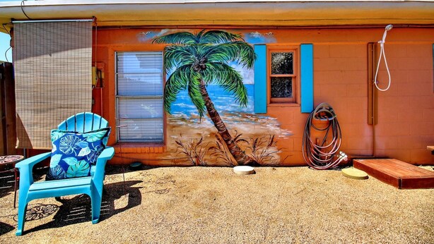 Ein Haus mit Wandgemälde einer Palme, einer Satellitenschüssel und einem blauen Stuhl.