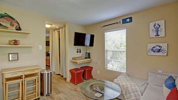 Una sala de estar con una mesa de centro de vidrio, un sofá, un televisor y una ventana con persianas.