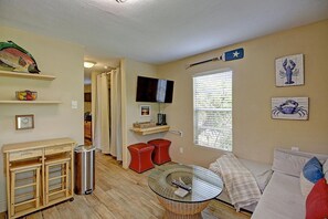 Ein Wohnzimmer mit Glastisch, einer Couch, einem Fernseher und einem Fenster mit Jalousien.