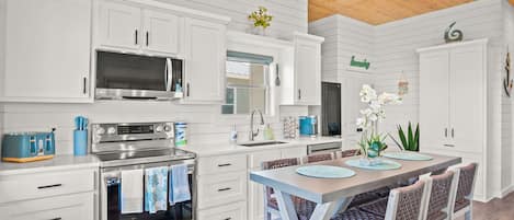 A modern kitchen with white cabinetry, stainless steel appliances, and a wooden ceiling.