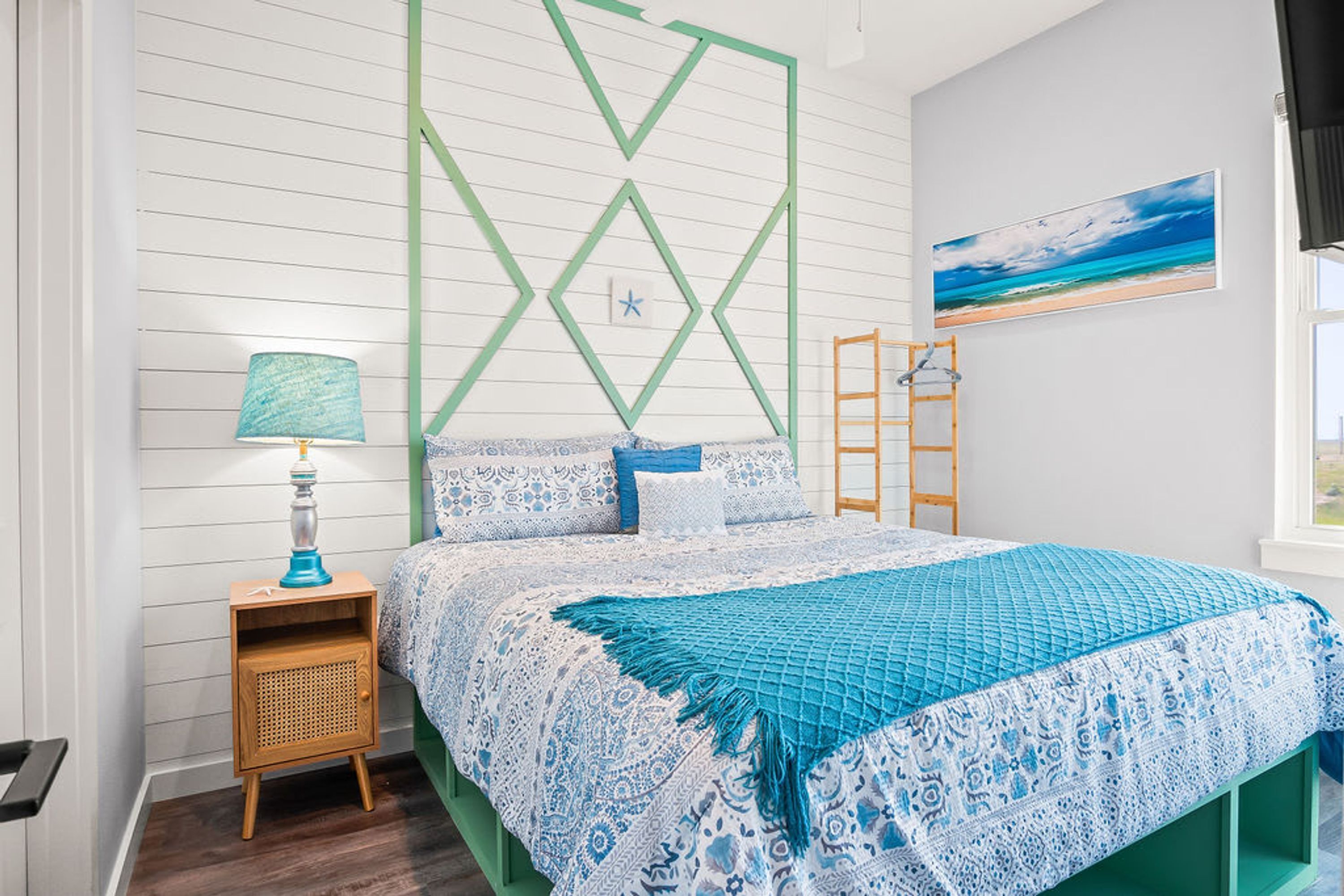 A bedroom with a bed, a nightstand, a lamp, a wall-mounted ladder, and a painting.
