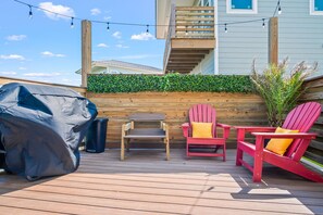 Una terraza de madera con mobiliario exterior, una parrilla y un muro cubierto de vegetación.