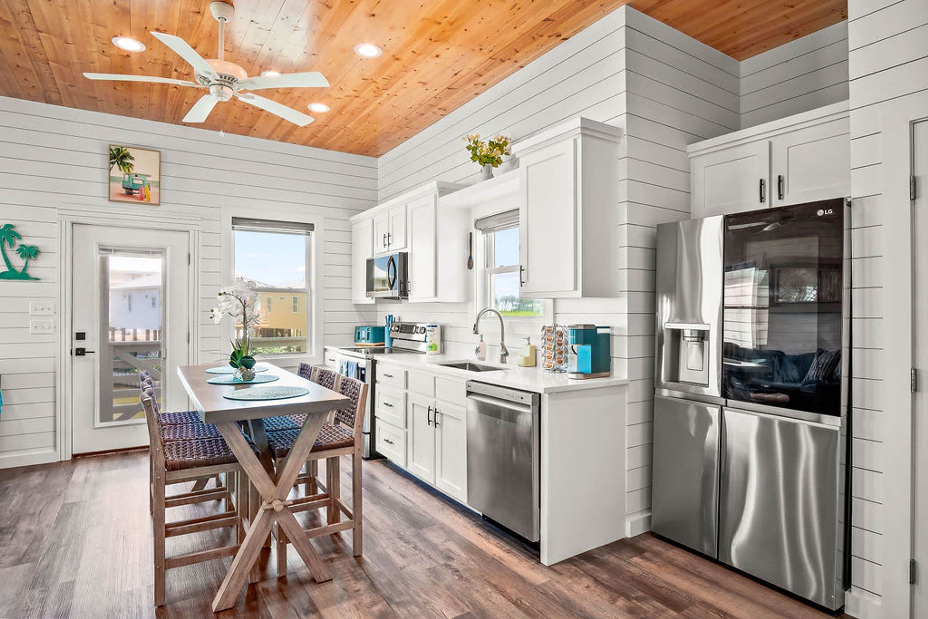 A modern kitchen with white cabinetry, a stainless steel refrigerator, and a ceiling fan.