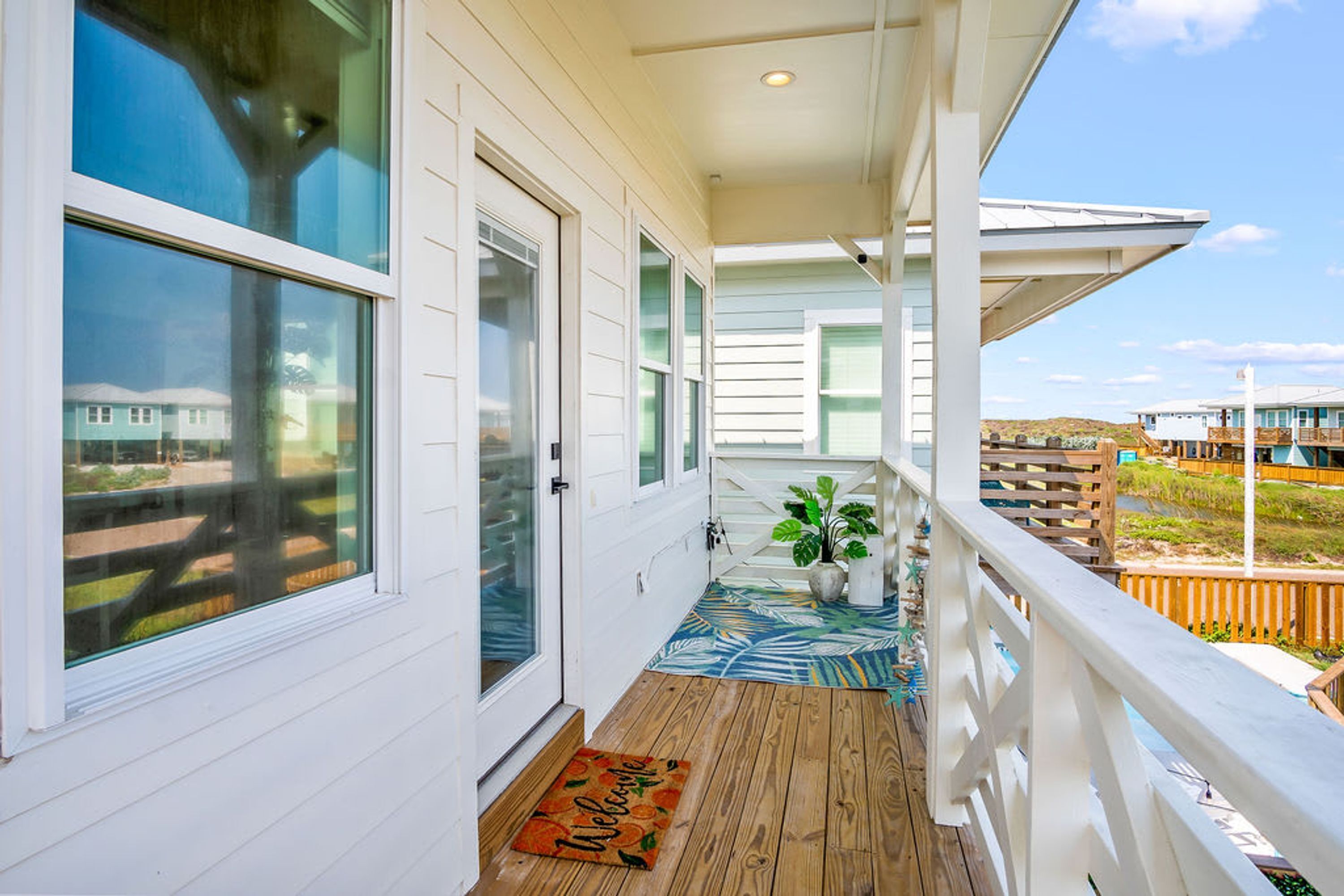 A covered porch with a wooden floor, a welcome mat, and a potted plant.