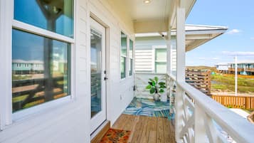 A covered porch with a wooden floor, a welcome mat, and a potted plant.