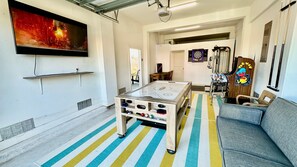 A room with a foosball table, a sofa, a dartboard, and a television mounted on the wall. - Mustang Island Beach Side Sanctuary Game Room (Port Aransas)