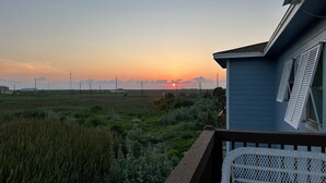 En boligejendom med udsigt til en solnedgang over et mark, en træterrasse og et lille skur.