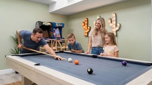A pool table with four people around it, a children's game machine, and a cactus decoration on the wall. - The Sunset Peak Sleeps 18 Heated Pool Hot Tub (Phoenix)