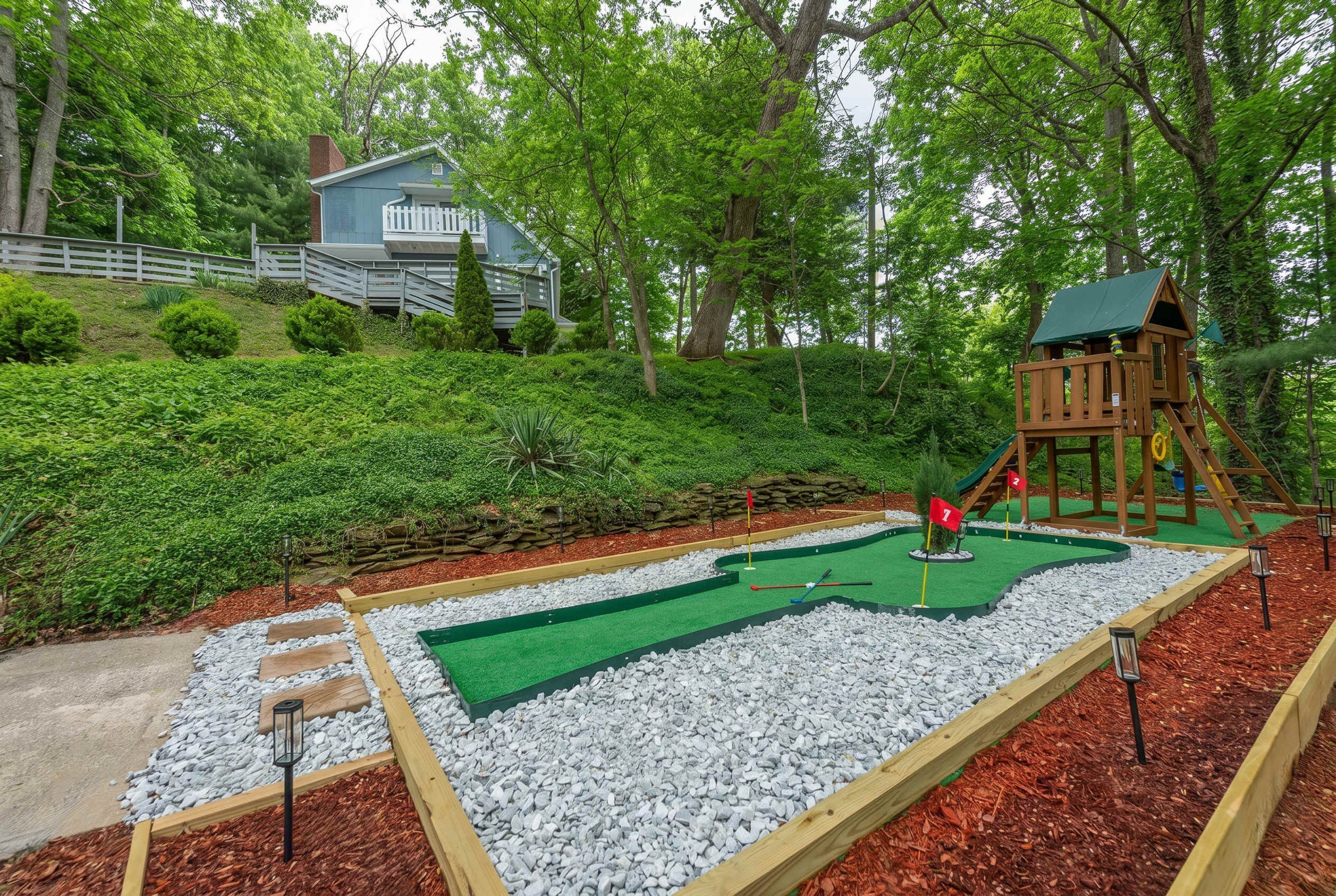A miniature golf course with a wooden playhouse and a house in the background.