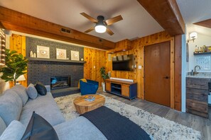 A cozy living room with a fireplace, a television, and a wooden wall. - 25 Min to Asheville Game Room Fire Pit Hot Tub (Arden)