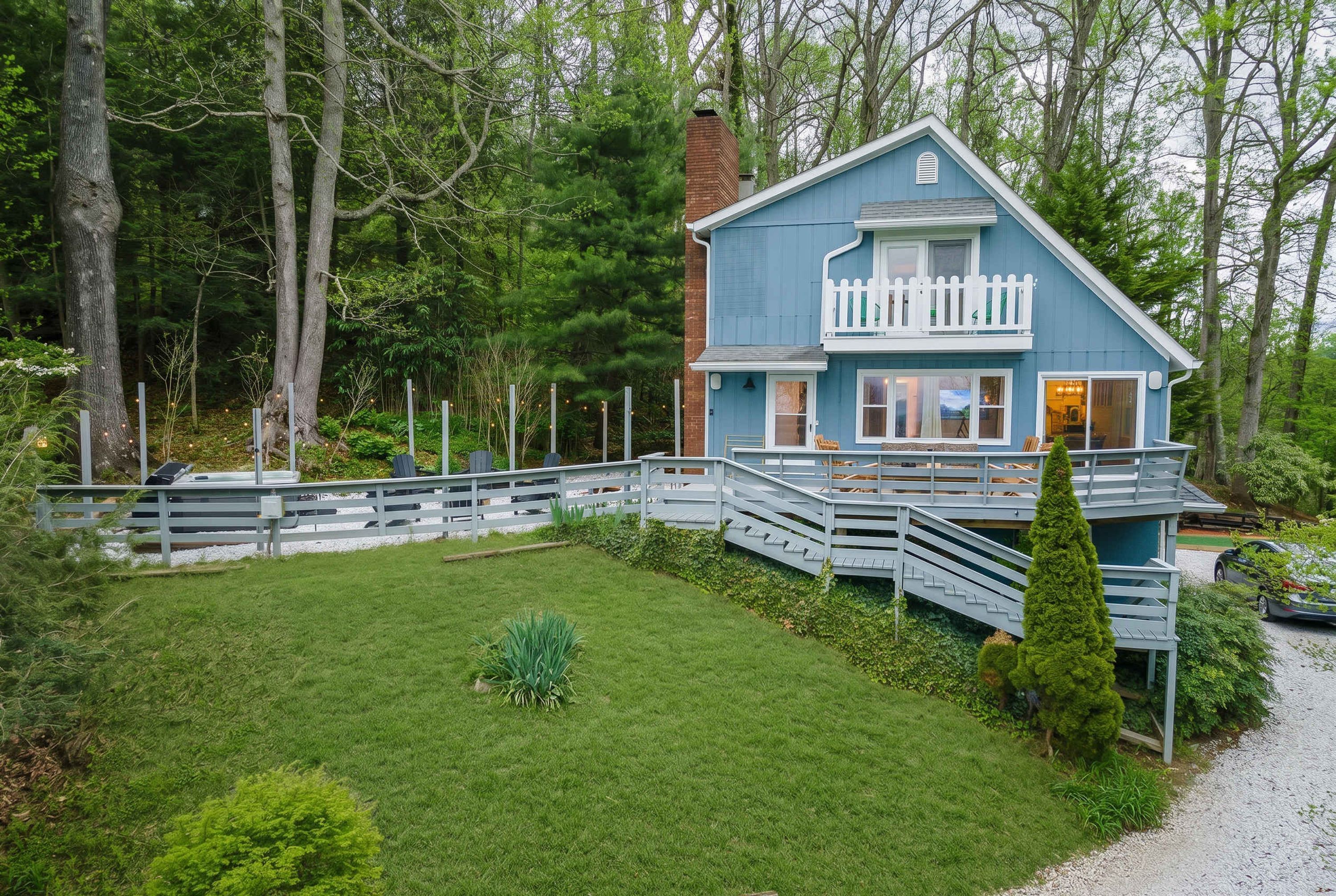 A two-story house with a blue exterior, a white porch, and a gravel driveway.
