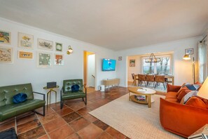 A living room with a television, green and orange sofas, a coffee table, and artwork on the walls. - 25 Min to Asheville Game Room Fire Pit Hot Tub (Arden)