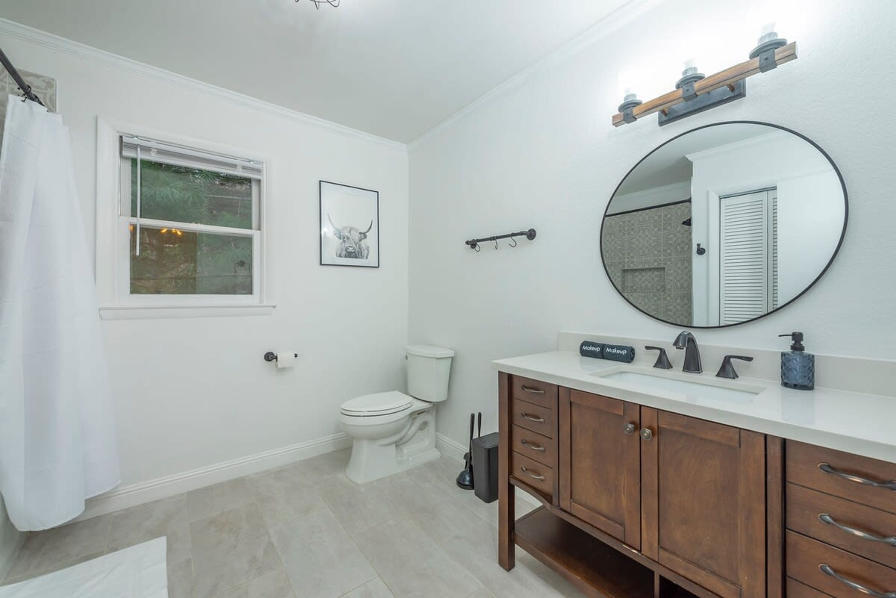 A bathroom with a toilet, a sink with a mirror, a shower curtain, and a framed picture on the wall.