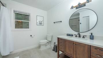 A bathroom with a toilet, a sink with a mirror, a shower curtain, and a framed picture on the wall.