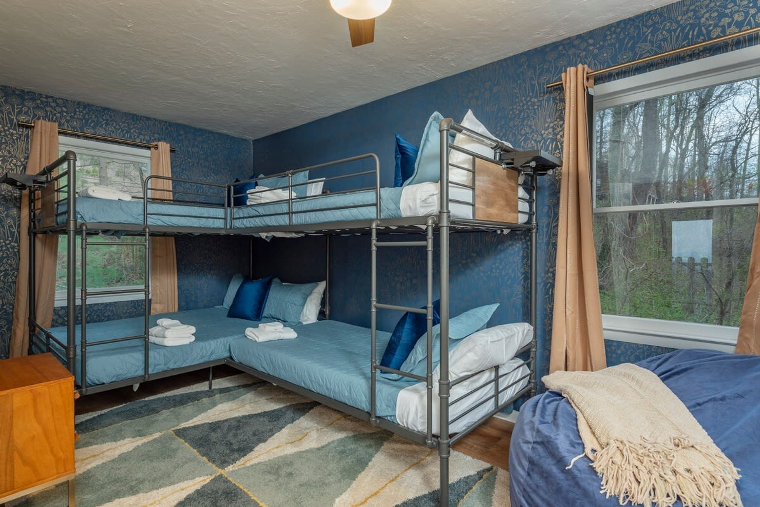 A bunk bed room with a window, a patterned rug, and a view of trees outside.