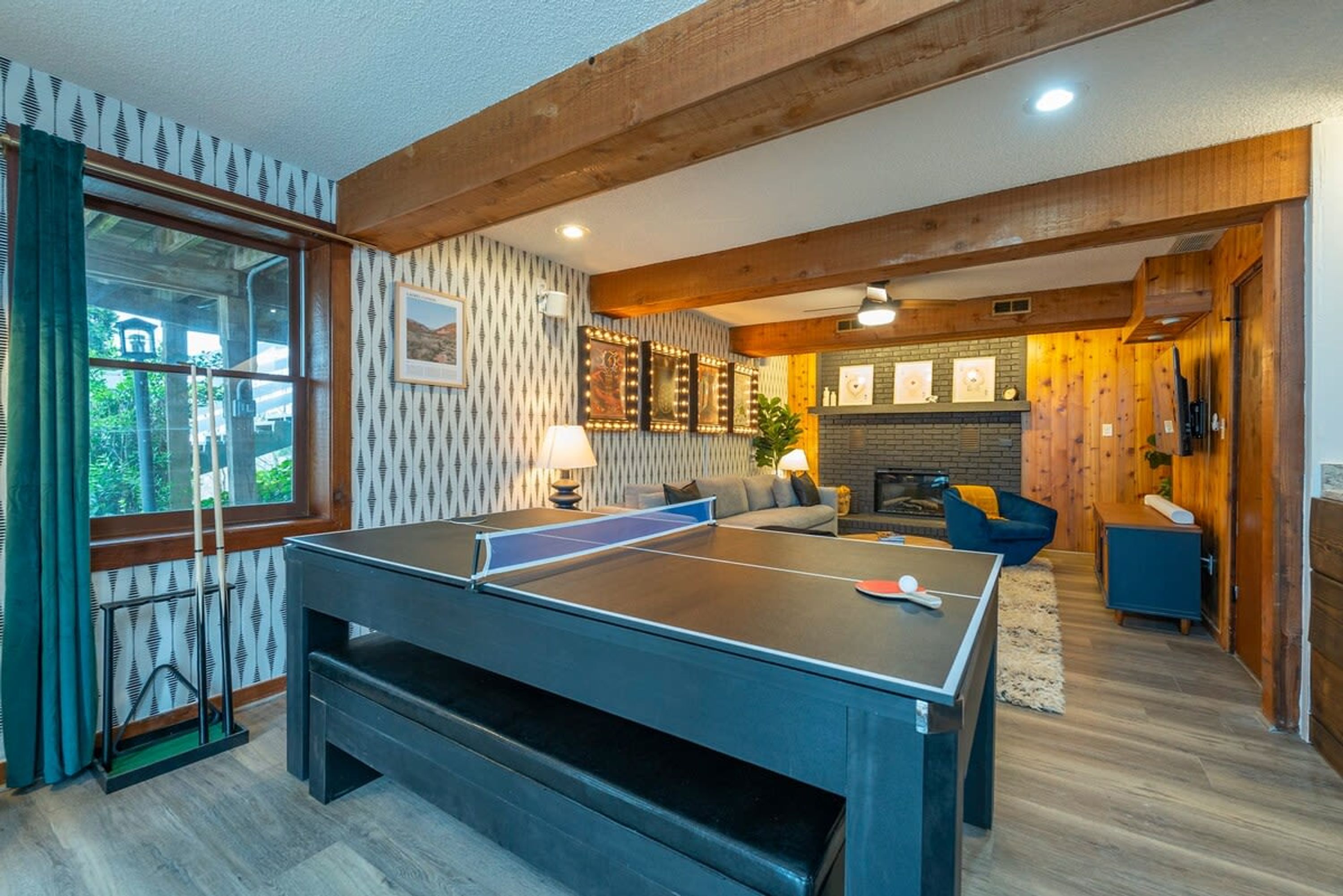 A room with a ping pong table, a sofa, a fireplace, and a window with curtains.