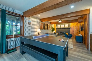 Una habitació amb taula de ping-pong, sofà, llar de foc i finestra amb cortines.
