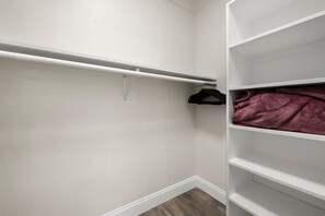 Un dressing avec des murs blancs, un plancher en bois et une tringle à vêtements sur laquelle est accroché un cintre noir.