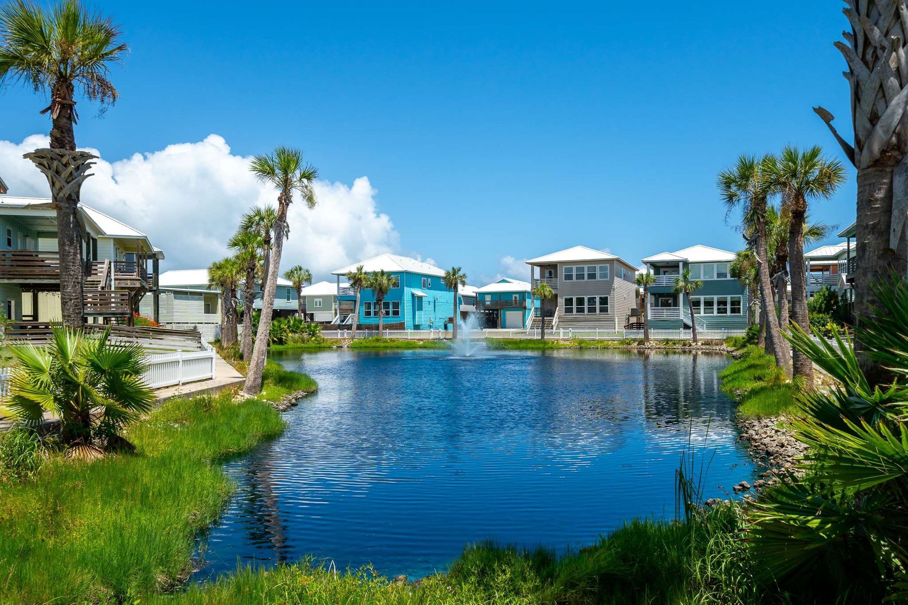 A waterfront property with a central pond, surrounded by palm trees and houses with blue and white exteriors.